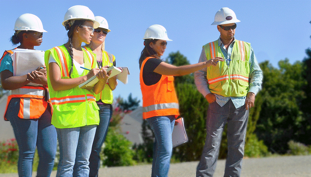 Four female construction workers in hi-vis vests and hard hats working with male construction worker