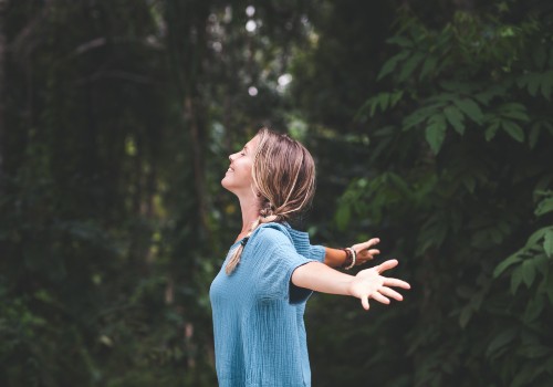 A woman with her arms wide open breathin in fresh air in a forest location. She is a patient of the counselling service at UC Health Clinics.